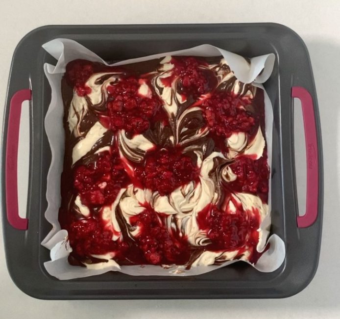 swirled cheesecake brownie mixture with raspberry dollops