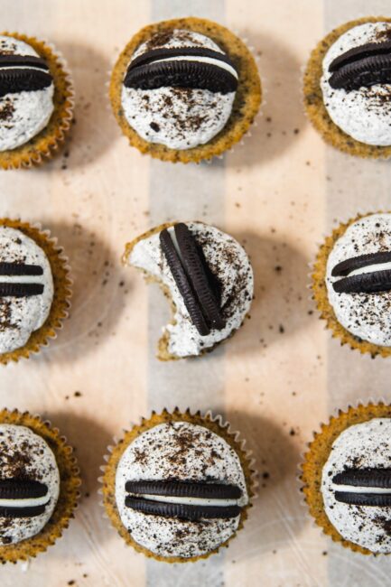 Oreo cupcakes (Oreo cookie sandwich on base, cookies and cream cupcake filling, and Swiss meringue buttercream as frosting) with bite taken out of centre cupcake.  Decorated with Oreo half and additional crushed chocolate cookie crumbs. 