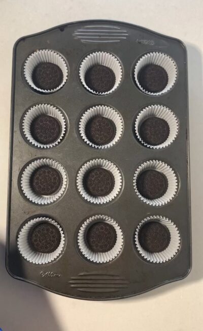 12 cupcake tin with paper liners and 1 Oreo cookie at the bottom of each