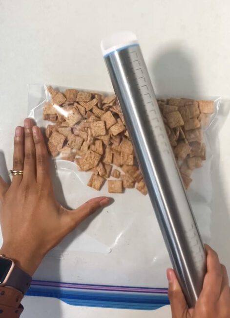 Cinnamon Toast Crunch in large zipper bag being crushed by stainless steel rolling pin