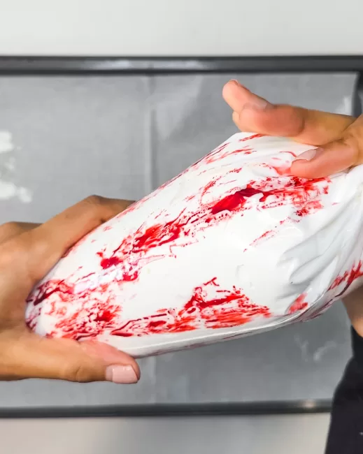 pipping bag of peppermint meringue with red food coloring streaks