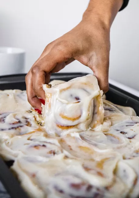 one Homemade Cinnamon Roll with cream cheese icing being taken from a fresh pan