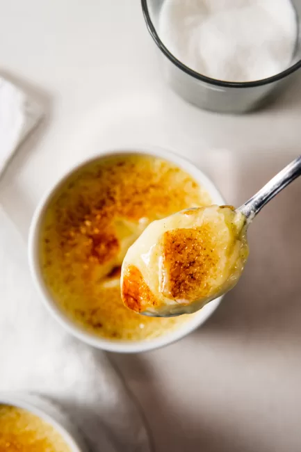 Crème Brûlée on a spoon above the ramekin