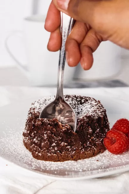 Chocolate Lava Cake with raspberries and icing sugar and a spoon taking a piece