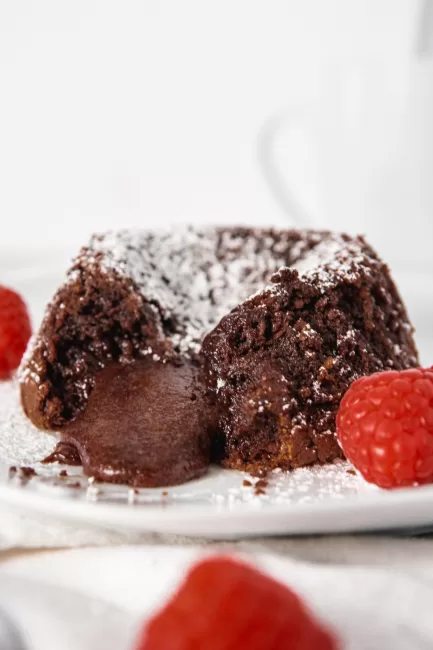 Chocolate Lava Cake with a piece missing, oozing chocolate with raspberries and icing sugar on top