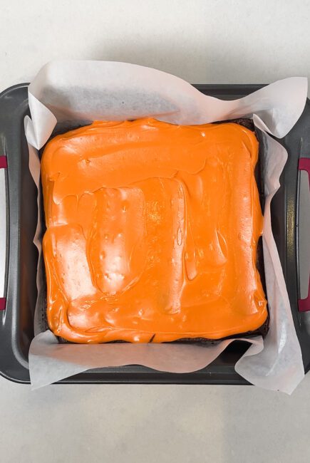 candy corn frosting spread on top of freshly baked brownies in a pan