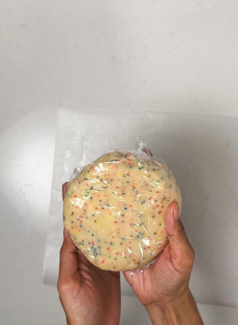 Birthday cake sugar cookie dough disk wrapped in plastic wrap ready for the refrigerator